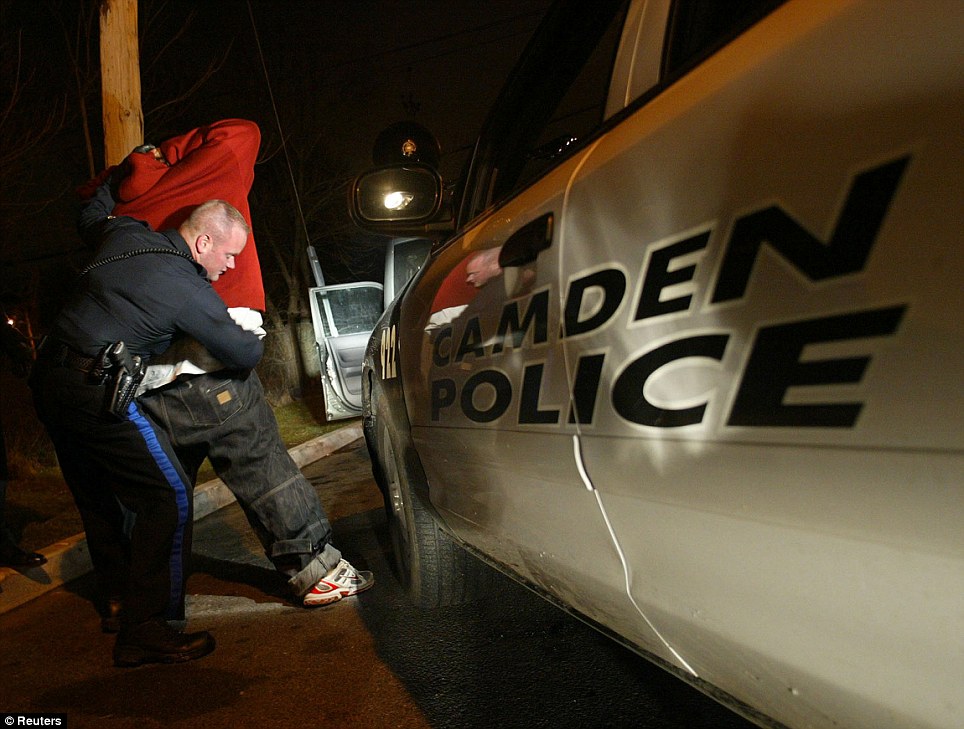 Streets of terror: A Camden police officer pats down a suspect. There were 13 homicides in the New Jersey city last month